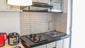 A compact kitchen with a gas stove, a sink, and a microwave. - Best View 2BR Apartment at Bassura City (Jakarta)