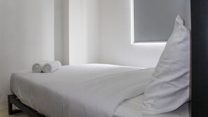 A minimalist hotel room with a neatly made bed, a window with blinds, and a clean, uncluttered space. - Comfy 2BR Apartment Bassura City near Shopping Mall (Jakarta)