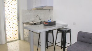 A compact kitchen with a white countertop, a stainless steel range hood, a sink, and two black bar stools. - Comfy 2BR Apartment Bassura City near Shopping Mall (Jakarta)