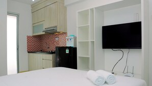 A hotel room with a bed, a TV mounted on the wall, a kitchen area with a refrigerator, and a water dispenser.