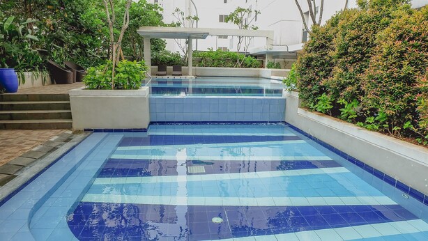 A swimming pool with a tiled deck, surrounded by greenery and a covered seating area.