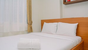 A neatly made bed with white linens and pillows, a rolled white towel, and a wooden headboard.