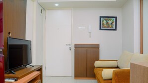 A room with a TV on a wooden stand, a wardrobe, a sofa with cushions, and a framed picture on the wall.