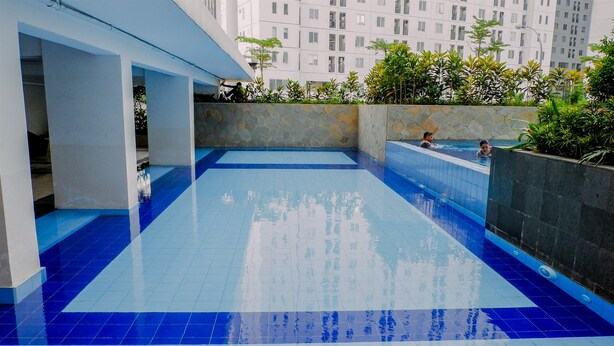 A rooftop swimming pool with blue tiles, surrounded by a stone wall and greenery. - 1BR Fully Furnished Bassura City Apartment (Jakarta)