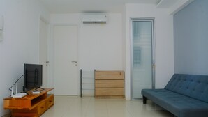A living room with a television on a wooden stand, a blue sofa, a wooden cabinet, and a glass door. - Best Deal 3BR Apartment Bassura City near Shopping Center (Jakarta)