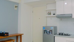 A compact kitchen with a refrigerator, a gas stove, and wooden stools. - Best Deal 3BR Apartment Bassura City near Shopping Center (Jakarta)