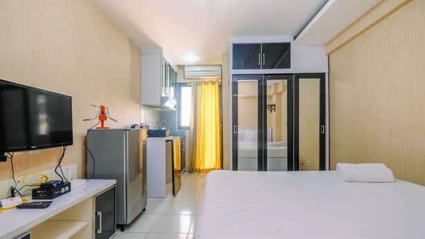 Una habitación de hotel con cama, escritorio con televisor, refrigerador y armario.