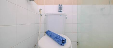 A toilet with a blue towel on the seat, a shower area, and tiled walls.