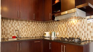 A kitchen with wooden cabinets, a tiled backsplash, a stainless steel sink, a toaster, and a stove. - Elegant 2BR at The Empyreal Condominium Epicentrum Apartment (Jakarta)