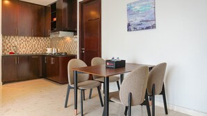 A compact kitchen with dark wooden cabinets, a tiled backsplash, and a dining table with four chairs. - Elegant 2BR at The Empyreal Condominium Epicentrum Apartment (Jakarta)