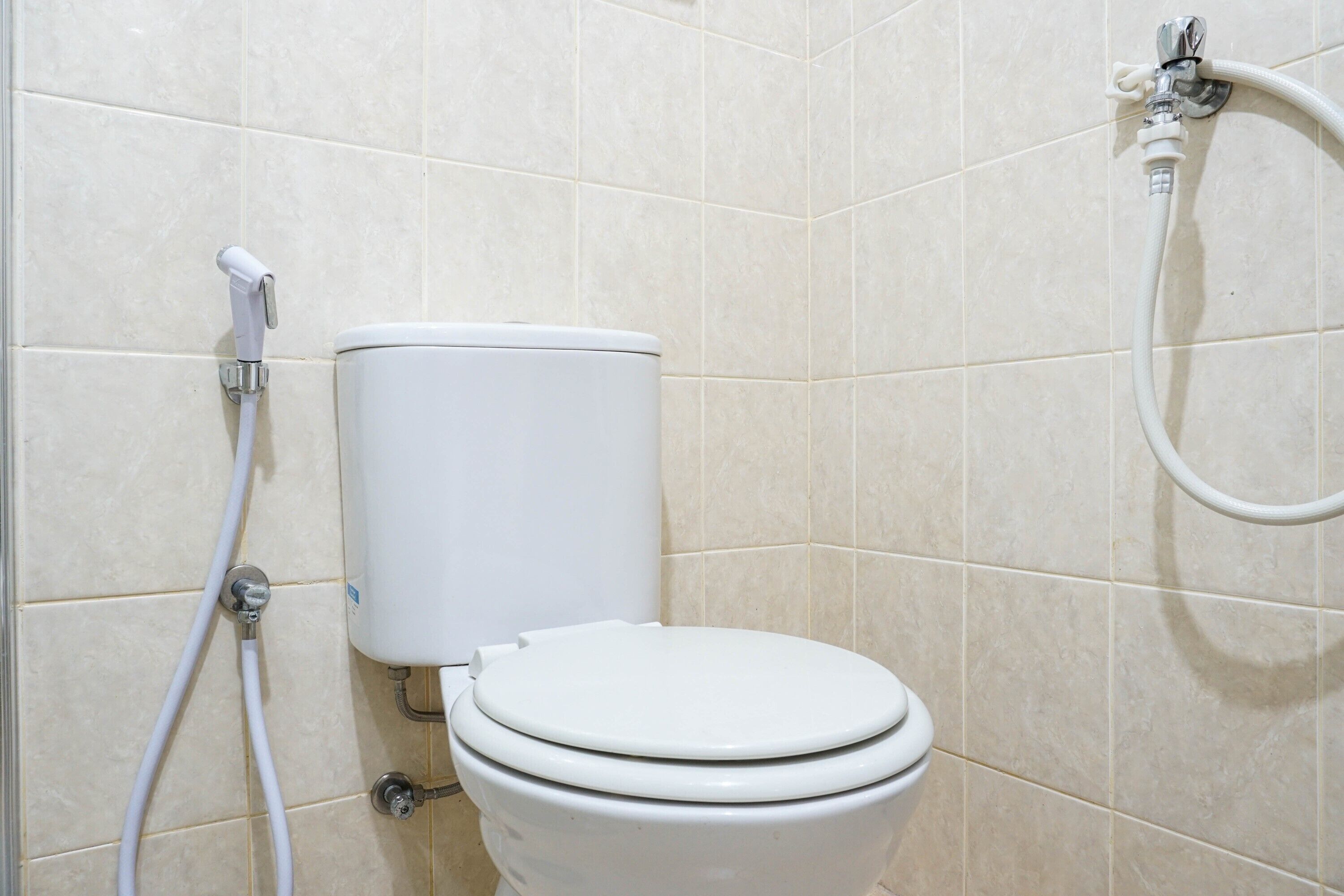 Des toilettes blanches avec une cuvette et un réservoir, un accessoire de type bidet et un tuyau.