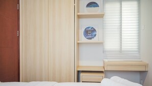 Ein Hotelzimmer mit Bett, Holzschrank, einer Ablage mit gerahmten Bildern und einem Fenster mit Jalousien.