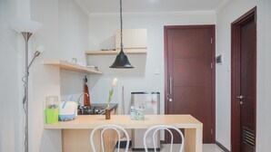 A compact kitchen with a central island, two white chairs, a hanging light fixture, and a refrigerator.