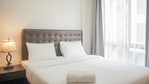 A hotel room with a large bed, two pillows, a bedside lamp, and a window with curtains.