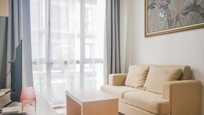A living room with a beige sofa, a white coffee table, and a television on a desk.