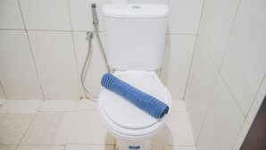 A white toilet with a blue towel on the seat, a toilet paper holder, and a shower hose.