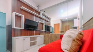 A modern living room with a red sofa, white cabinets, and a flat-screen TV mounted on a wooden wall. - Minimalist & Comfy 2BR @ Titanium Square Apartment (Jakarta)