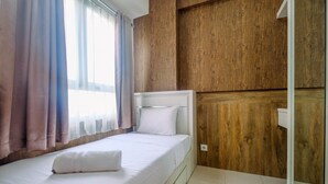 A neatly made bed with white linens and a white pillow, a wooden wall paneling, and a window with sheer curtains. - Minimalist & Comfy 2BR @ Titanium Square Apartment (Jakarta)