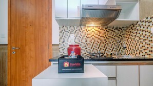 A kitchen with a tiled backsplash, a stove, a sink, and a travel bag labeled 'Travelio Property Management' on a counter. - Minimalist & Comfy 2BR @ Titanium Square Apartment (Jakarta)