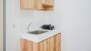A small kitchen with a white countertop, a stainless steel sink, wooden cabinets, and a portable electric stove. - Simply and Homey 1BR Apartment at M Town Residence (Gading Serpong)