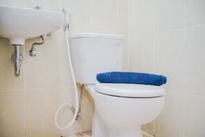 A white toilet with a blue towel on top, a white sink, and a visible toilet paper holder. - Simply and Homey 1BR Apartment at M Town Residence (Gading Serpong)