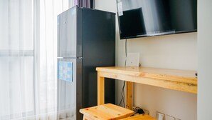 A compact kitchen with a black refrigerator, wooden stools, a wooden table, and a mounted TV. - Simply and Homey 1BR Apartment at M Town Residence (Gading Serpong)