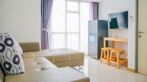 A modern living room with a sofa, a small wooden table, and a television mounted on the wall. - Simply and Homey 1BR Apartment at M Town Residence (Gading Serpong)
