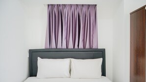 A bed with a grey headboard and white bedding, a purple curtain, and a wooden wardrobe. - Simply and Homey 1BR Apartment at M Town Residence (Gading Serpong)