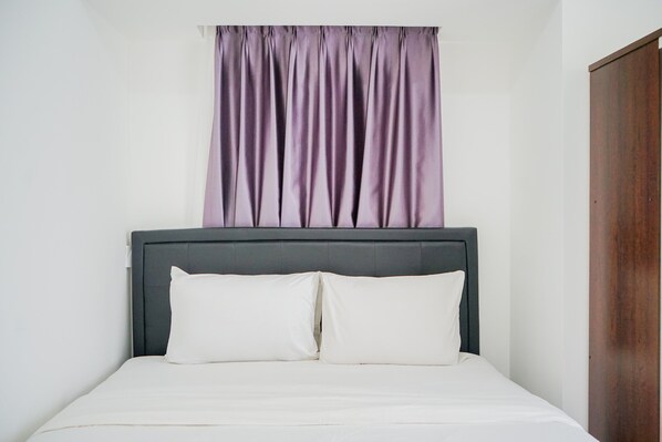 A bed with a grey headboard and white bedding, a purple curtain, and a wooden wardrobe. - Simply and Homey 1BR Apartment at M Town Residence (Gading Serpong)