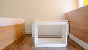 Una camera da letto con un letto in legno, un comodino bianco e un pavimento in legno.