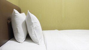 Cama com lençóis e duas almofadas brancas, com uma parede amarela ao fundo.