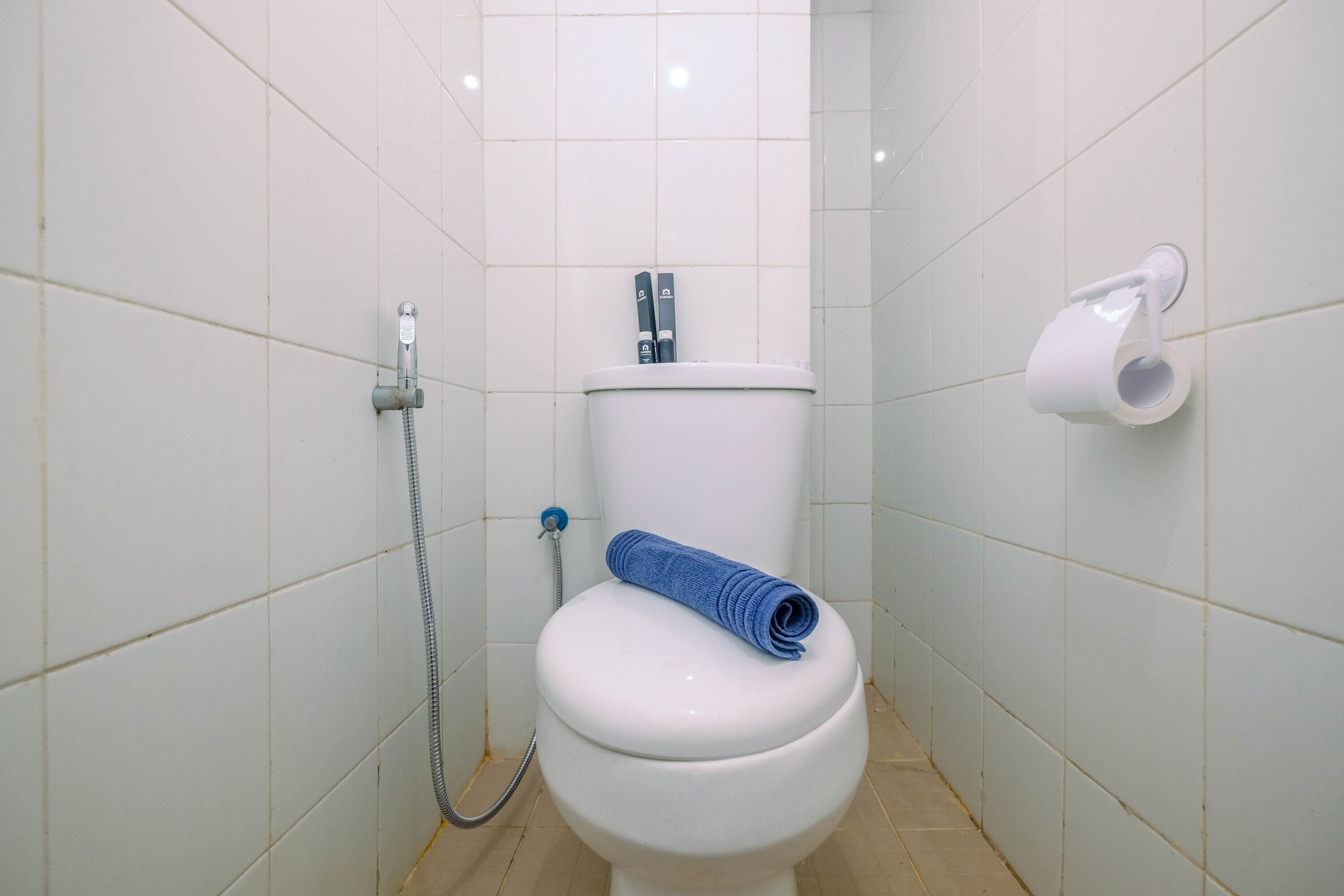 Un baño con inodoro blanco, ducha y dispensador de papel higiénico en la pared.