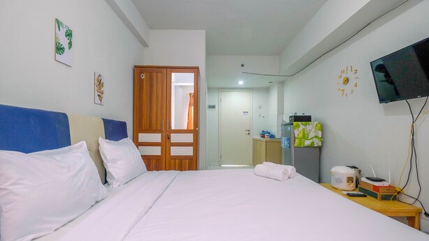 Een hotelkamer met een bed, een houten garderobe, een televisie en een kleine tafel met een afstandsbediening en een rijstkoker.