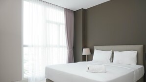 Una camera d'albergo moderna con un letto grande, un comodino con una lampada e tende leggere alla finestra.