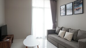 Un soggiorno moderno con un divano grigio, un tavolo bianco e una TV su un mobile in legno. Tre quadri appesi alla parete.