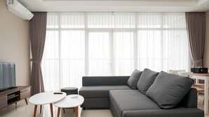 A modern living room with a grey sofa, two round tables, a TV, and a dining area with a table and chairs.