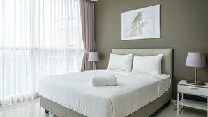 A modern hotel room with a large bed, a bedside table, a lamp, and a window with sheer curtains.