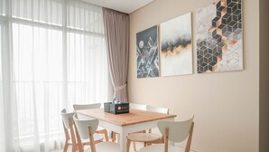 A dining area with a wooden table and white chairs, a window with sheer curtains, and three wall art pieces.