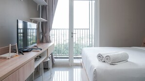 A hotel room with a bed, a desk with a computer, a TV, and a balcony with a view. - Comfortable Design Studio Apartment Ciputra International (Jakarta)