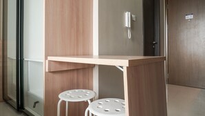 A small wooden desk with two white stools, a telephone, and a door with a sign. - Comfortable Design Studio Apartment Ciputra International (Jakarta)
