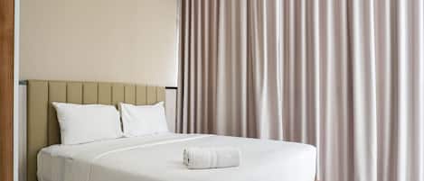 A neatly made bed with a white duvet, a wooden headboard, and a rolled white towel on the bed.