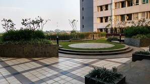 A courtyard with tiled flooring, planters with various plants, and a building in the background.