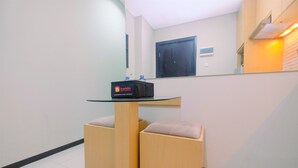 A small, modern room with a glass-top table, two wooden ottomans, and a black suitcase on the table.