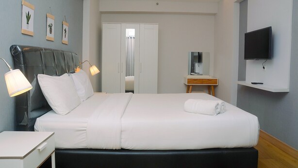 A neatly arranged hotel room with a bed, bedside table, lamp, TV, and a wardrobe. - Minimalist with City View 2BR Apartment at Casablanca East Residences (Jakarta)