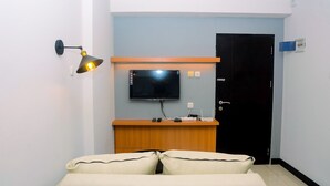 A hotel room with a bed, a desk with a flat-screen TV, a wall-mounted lamp, and a door. - Minimalist with City View 2BR Apartment at Casablanca East Residences (Jakarta)