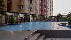 A swimming pool surrounded by a multi-story residential building with balconies. - Minimalist with City View 2BR Apartment at Casablanca East Residences (Jakarta)