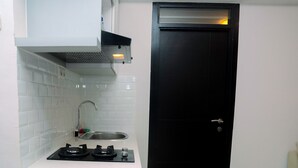 A compact kitchen with white tiles, a gas stove, a sink, and a black door. - Minimalist with City View 2BR Apartment at Casablanca East Residences (Jakarta)