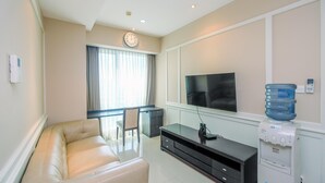 Una sala moderna con un sofá, un televisor de pantalla plana, un dispensador de agua y un escritorio con una silla.