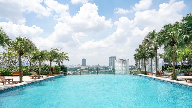 Una piscina con sillones de descanso y palmeras, rodeada de edificios altos.