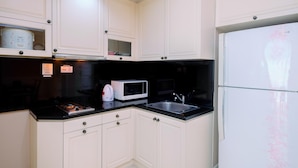 Una cocina con armarios blancos, encimera negra, microondas, estufa y refrigerador.
